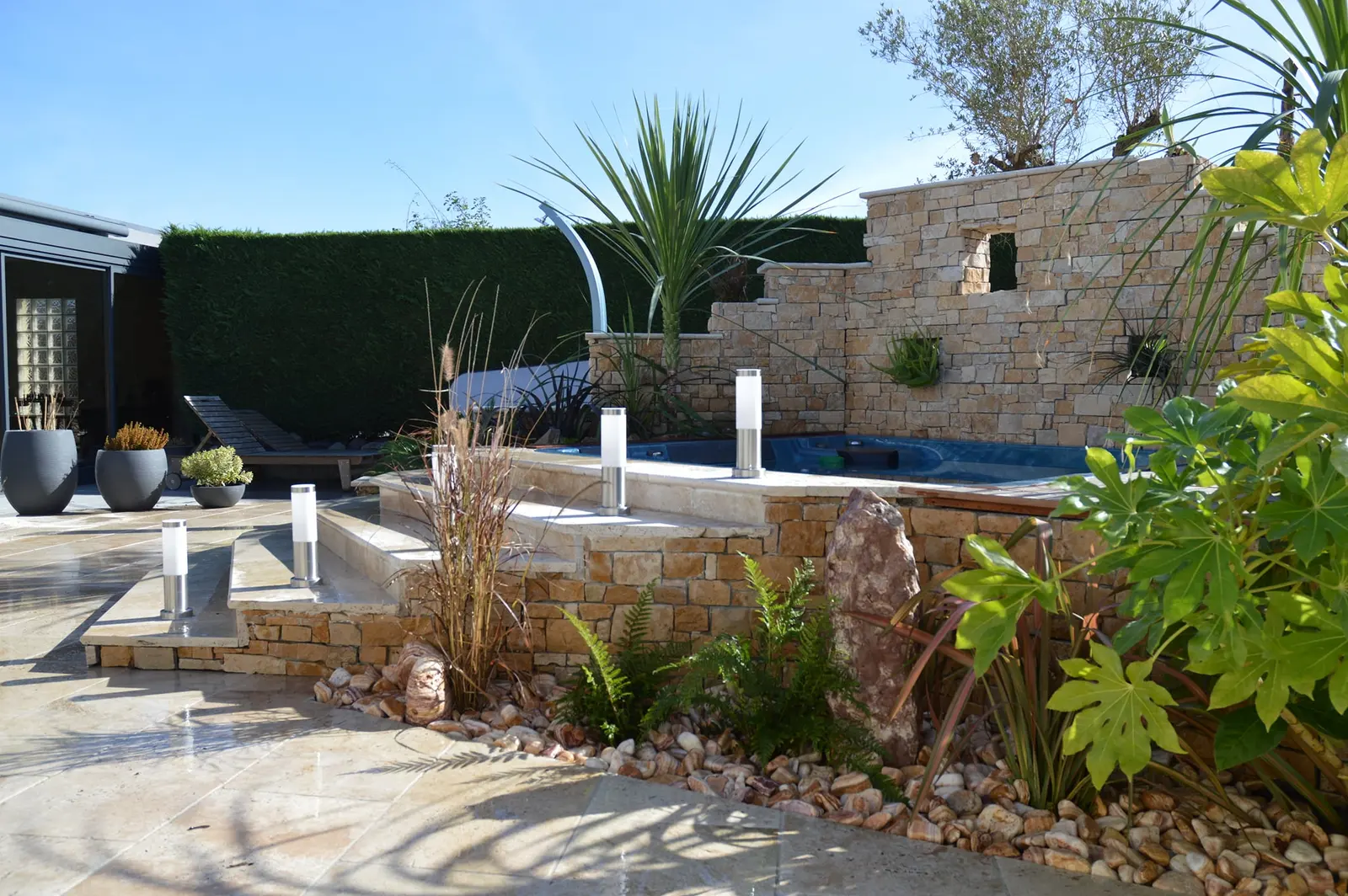 Terrasse et piscine avec mur en pierre et palmiers, réalisation Aux Jardins d’Elisa
